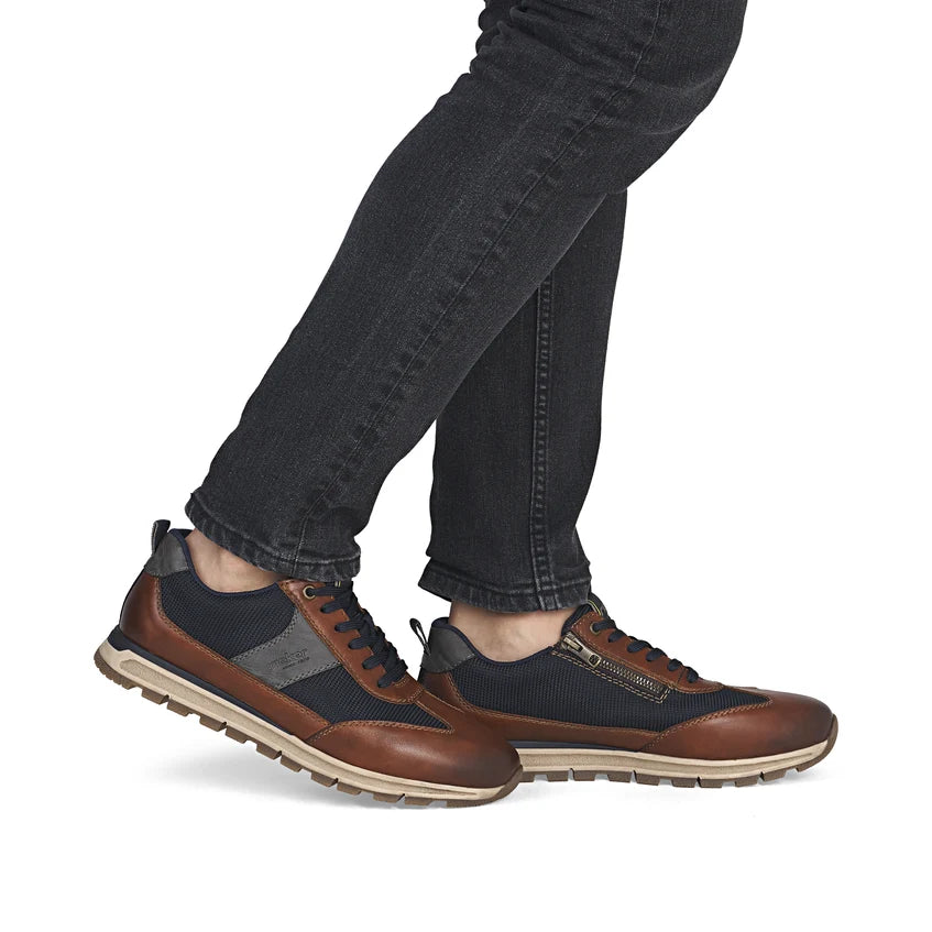 Men's brown and navy leather trainer worn with dark jeans, lace-up and thick sole