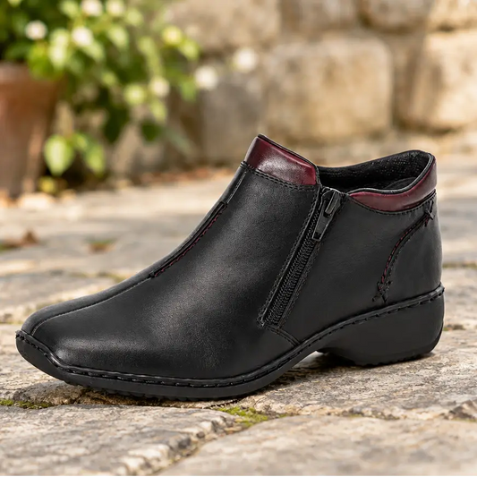Women’s black leather ankle boot on stone with side zipper and red accents