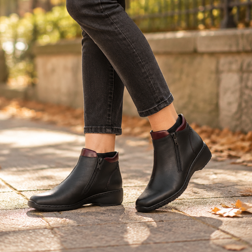 Women’s black leather ankle boot worn with dark pants and red collar detail