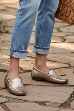 Person wearing metallic loafers and blue jeans on a stone pavement