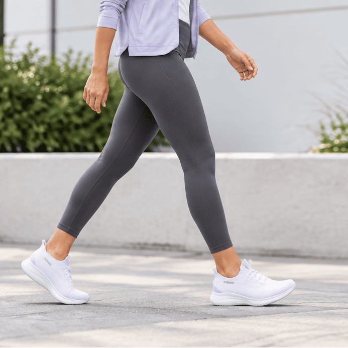 Women's white trainer with knit upper and elastic collar, walking stance