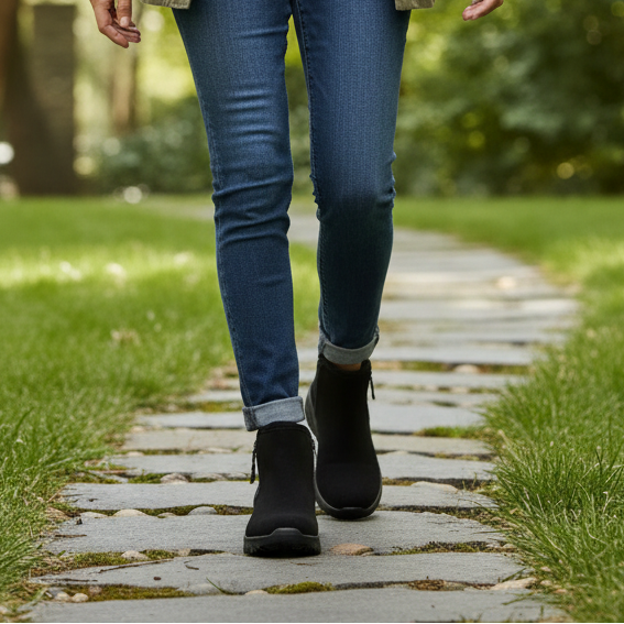 Black ankle boots on feet with blue jeans on a paved path