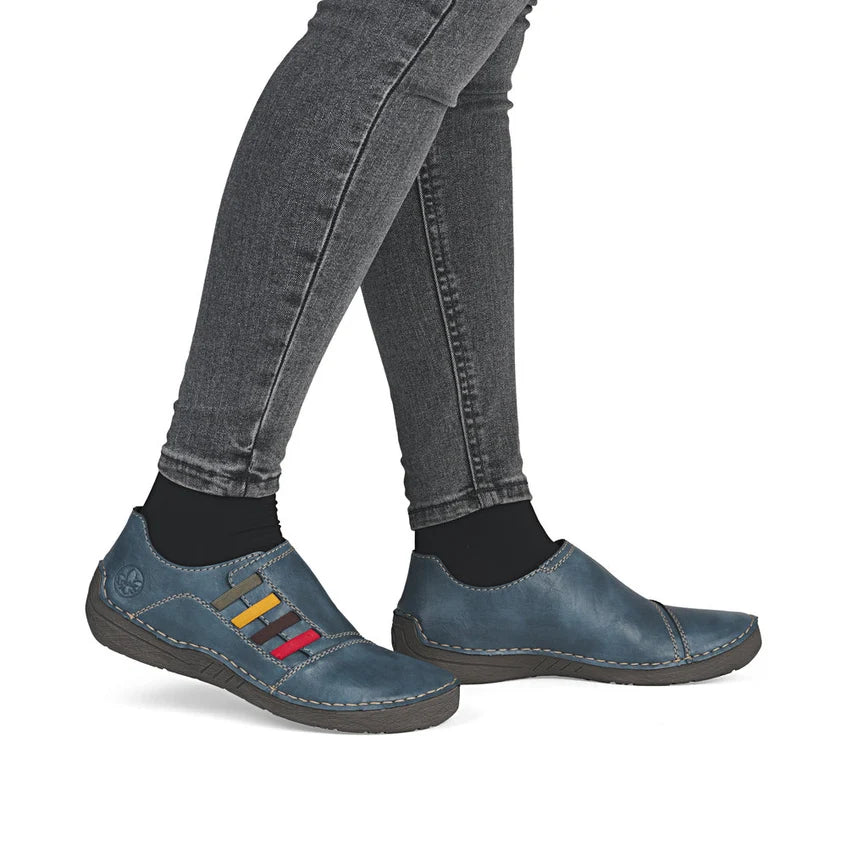 Blue slip-on shoes with colorful stripe accents and stitched detailing, with jeans