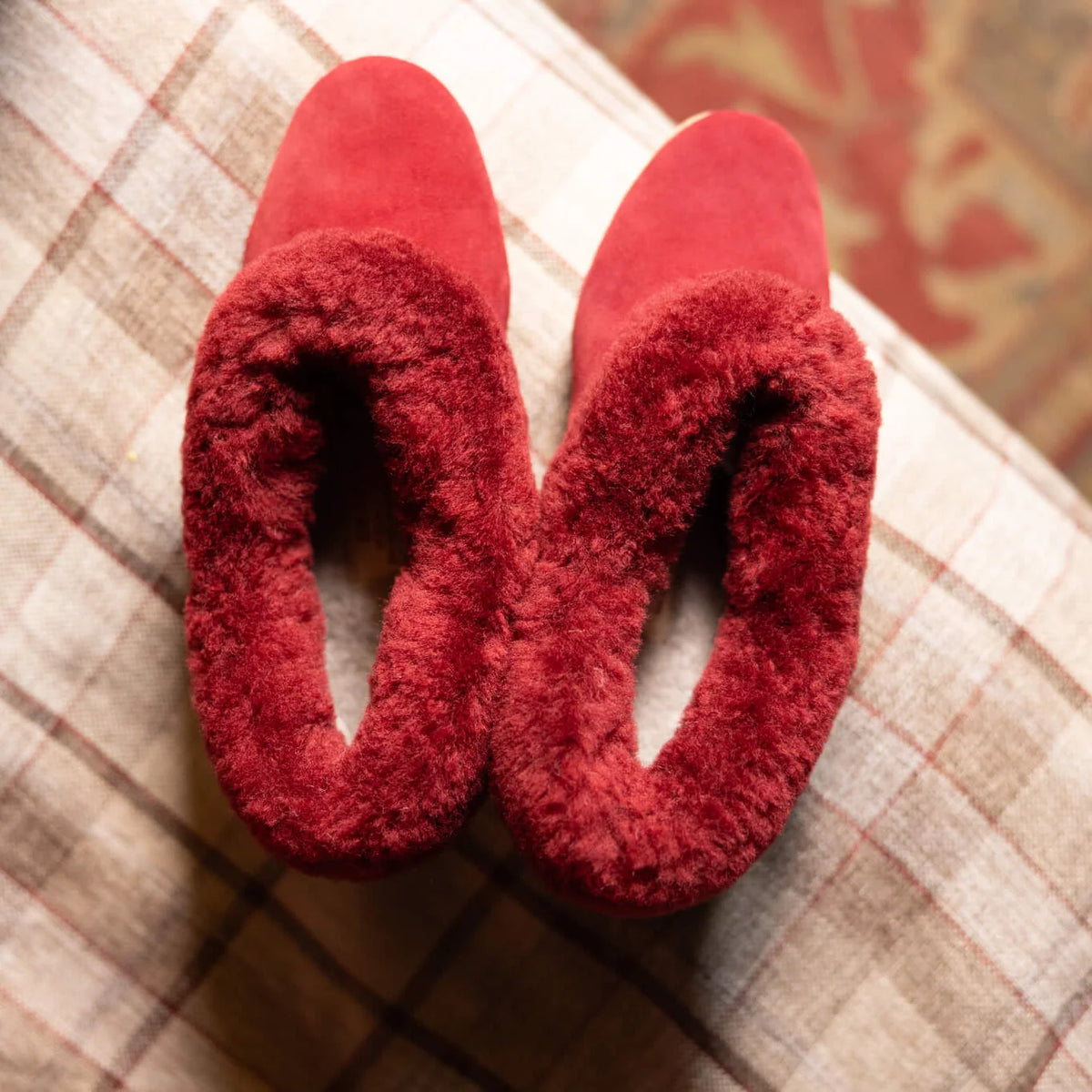 Cherry red sheepskin slippers close-up on a plaid fabric surface