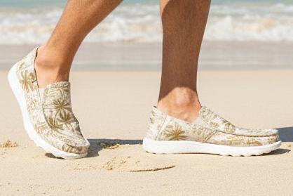Person walking on a sandy beach with clear blue water and sky.