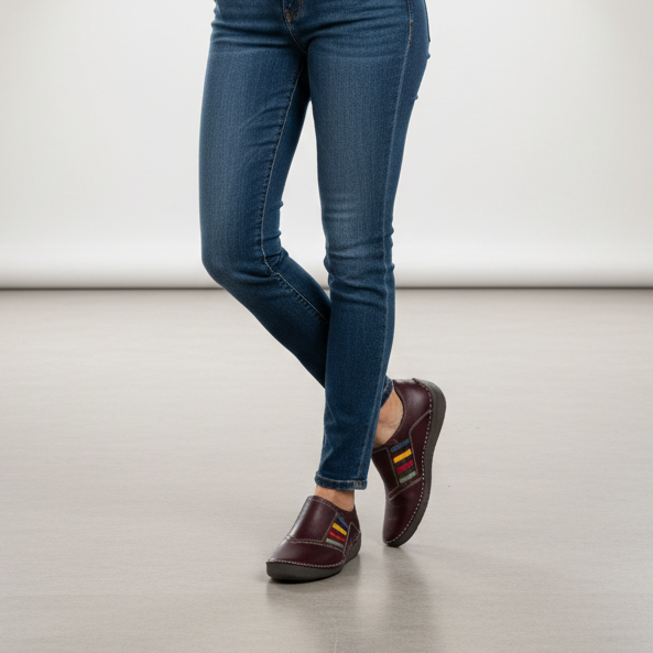 Women's slip-on shoes dark plum worn with jeans, multicolor strap detail visible