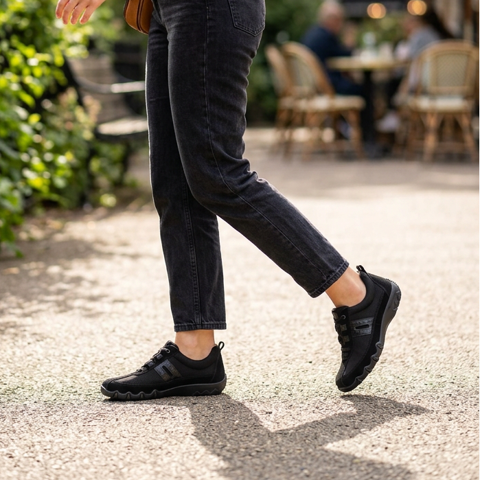 Black lace-up trainers worn with dark jeans on a paved outdoor path